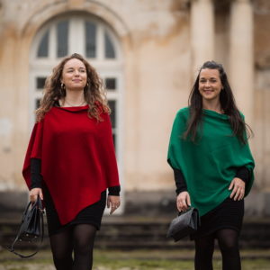 Ponchos en 100% mérinos extrafin portés par deux femmes marchant vers la caméra. La femme de gauche porte le ponch de couleur rouge et la femme de droite porte le poncho de couleur vert profond.